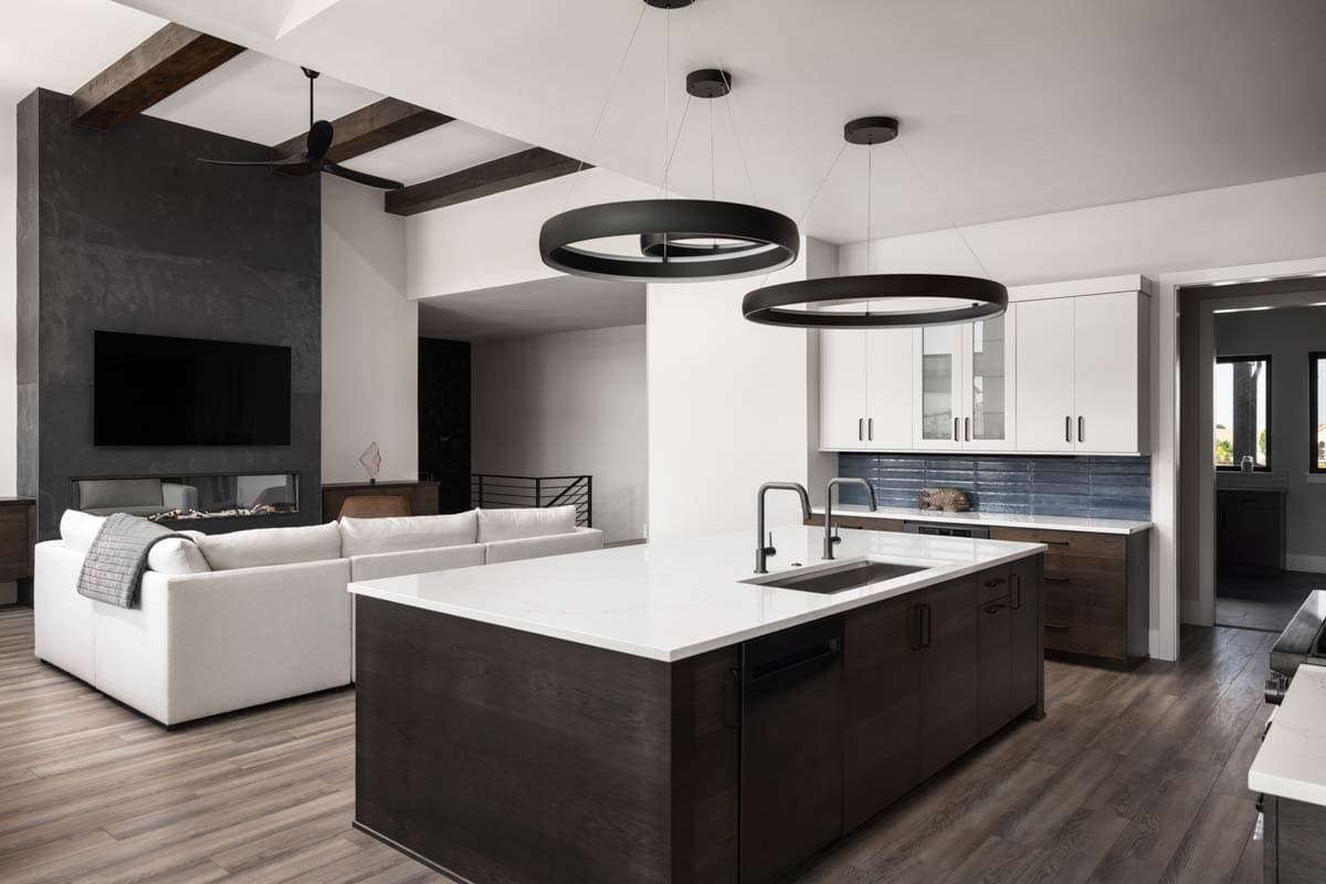 Modern kitchen with dark wood island, white cabinetry, tile backsplash, and open living area with fireplace and media center.