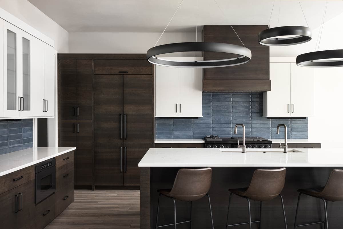 Kitchen with dark wood cabinets, white upper cabinets, island with seating, blue tile backsplash, and modern pendant lights.