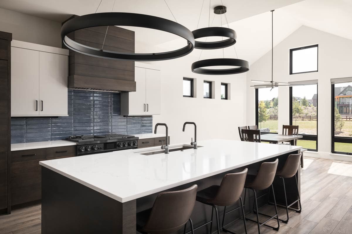Modern kitchen with large island, dark wood cabinetry, white counters, blue subway tile backsplash, and island pendant lights.