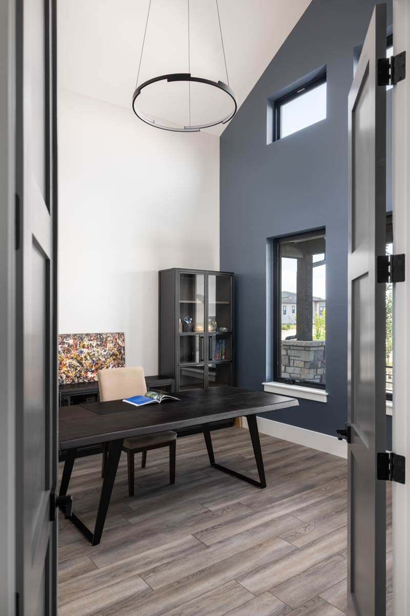 Office with desk, chair, cabinet, artwork, and high ceiling with modern circular light fixture.