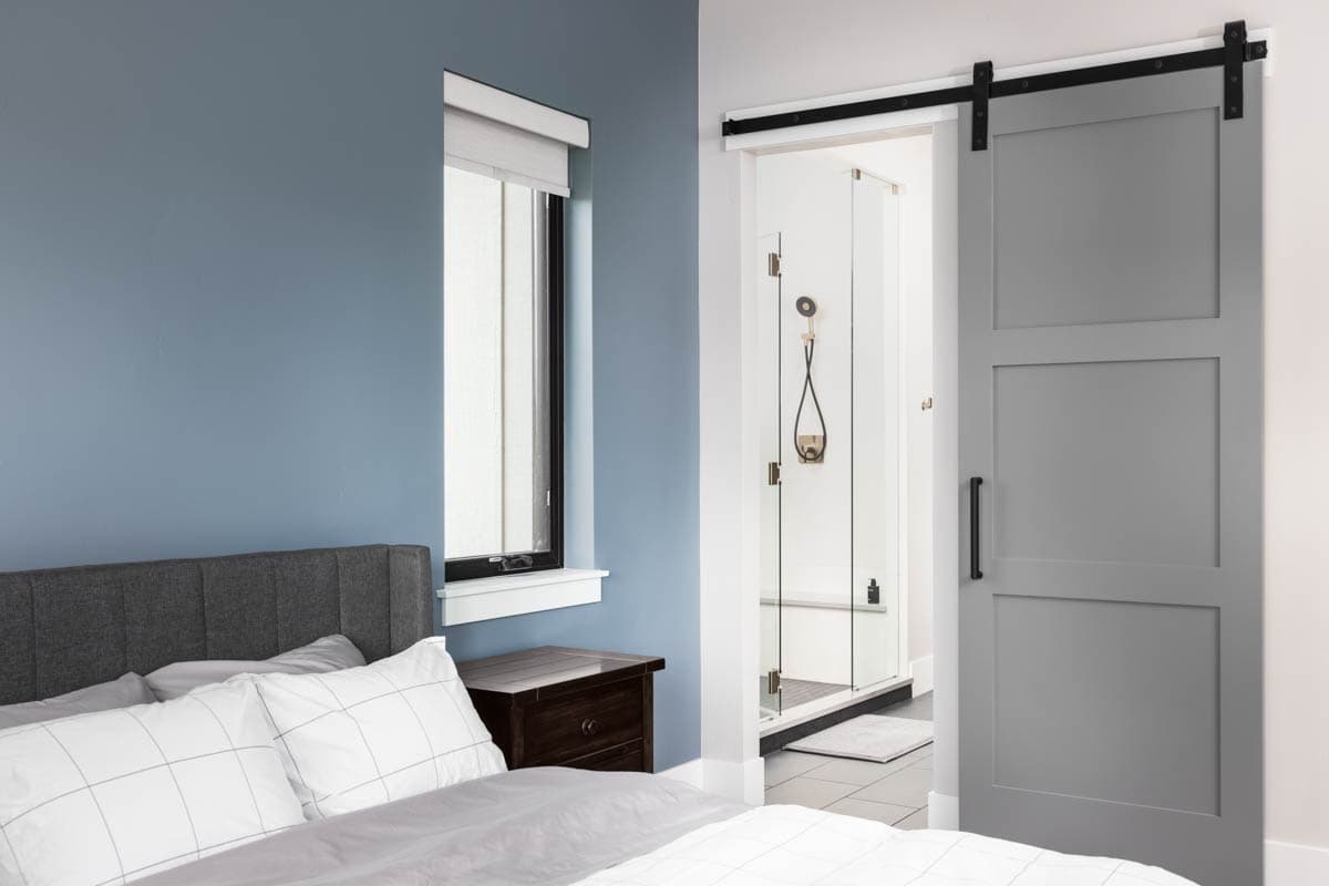 Bedroom with blue walls and gray barn door to glass-enclosed shower.