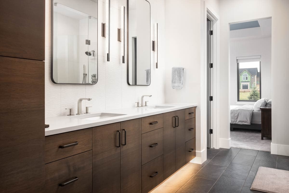 Modern bathroom with double vanity, white tile backsplash, and brushed nickel fixtures. Adjacent bedroom visible through doorway.