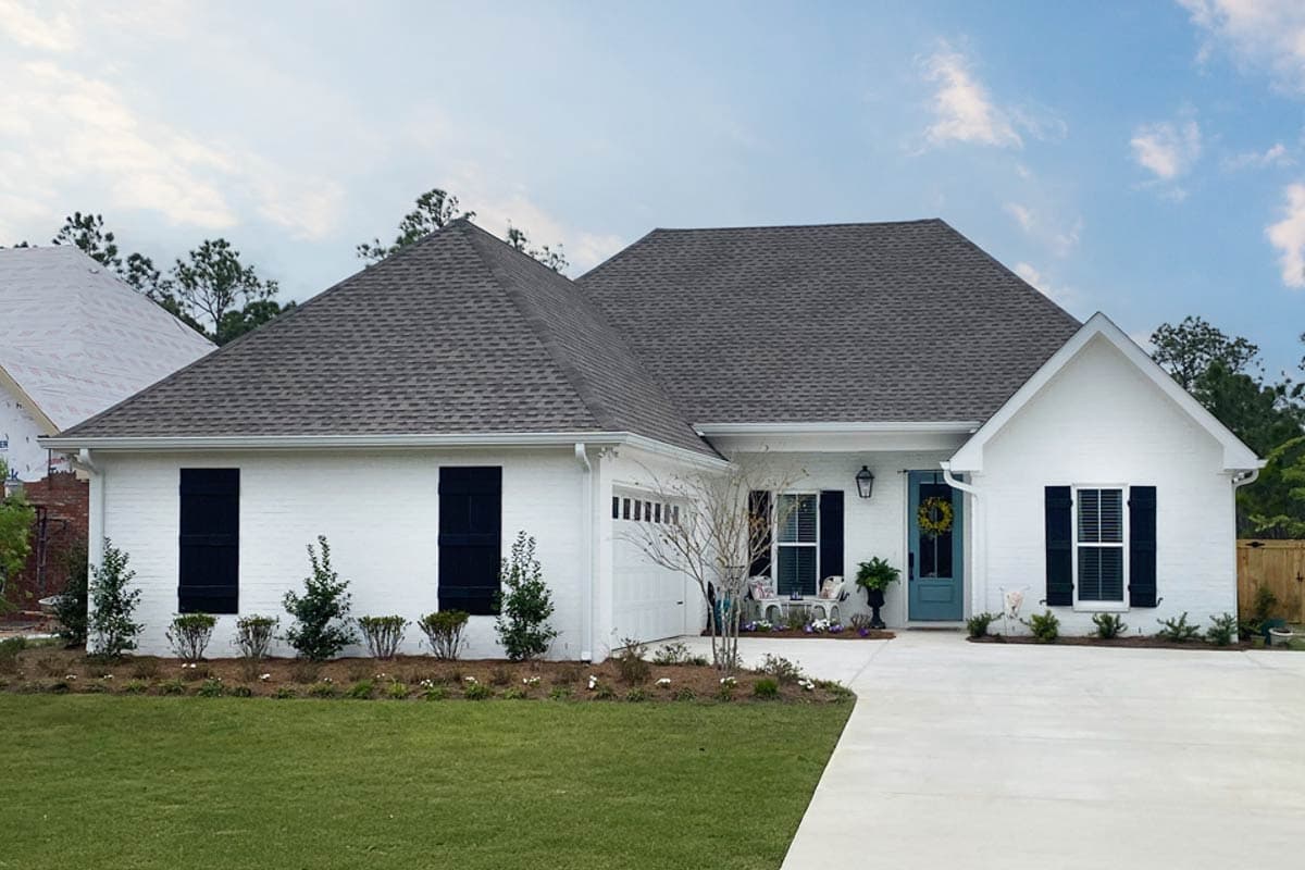 House plan exterior. One-story Ranch style home with a gable roof, garage, and black shutters on the windows.