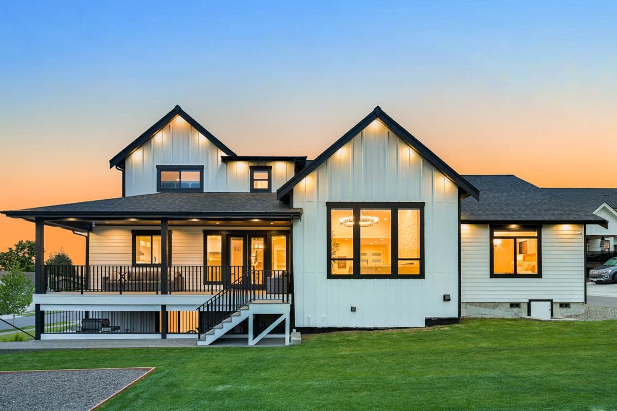 Modern Farmhouse house plan exterior with white board and batten siding, dark gables, wraparound porch, and large windows.
