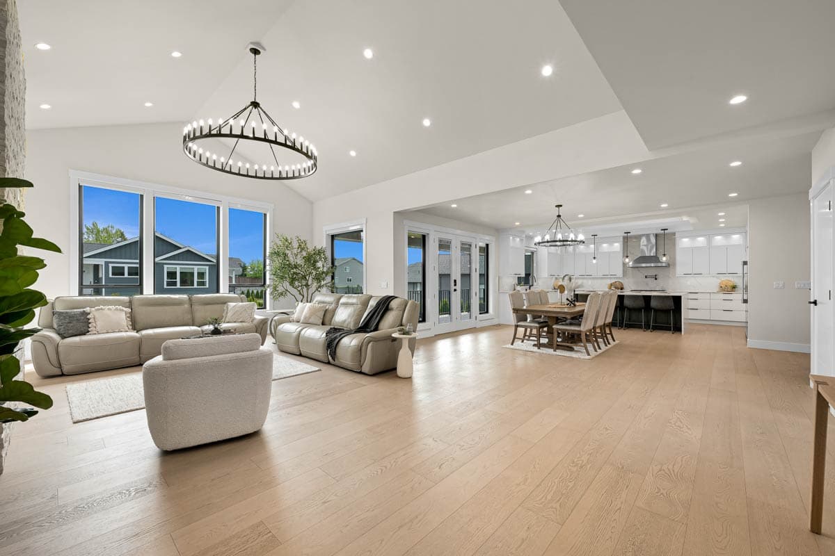 Open concept living space with vaulted ceiling, large windows, modern kitchen with island, and dining area.