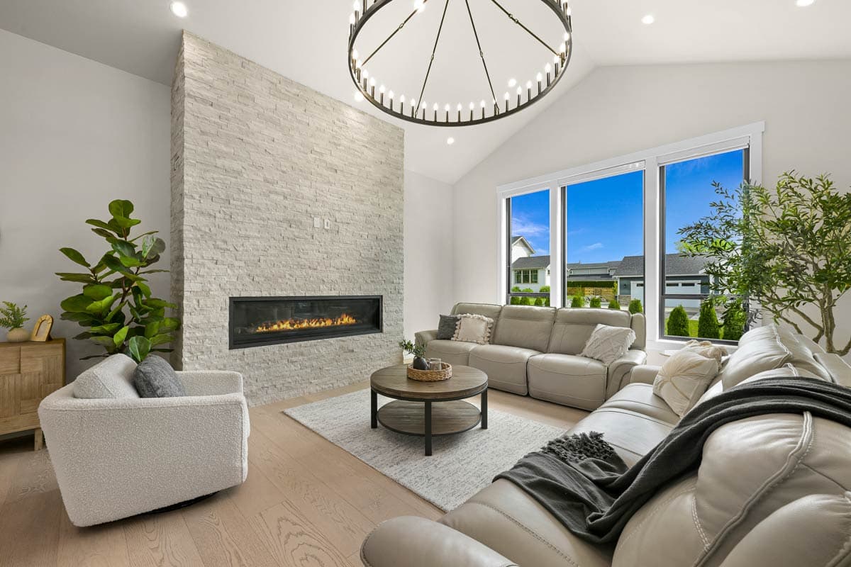 Living room with vaulted ceiling, stacked stone fireplace, sectional sofa, and large windows.