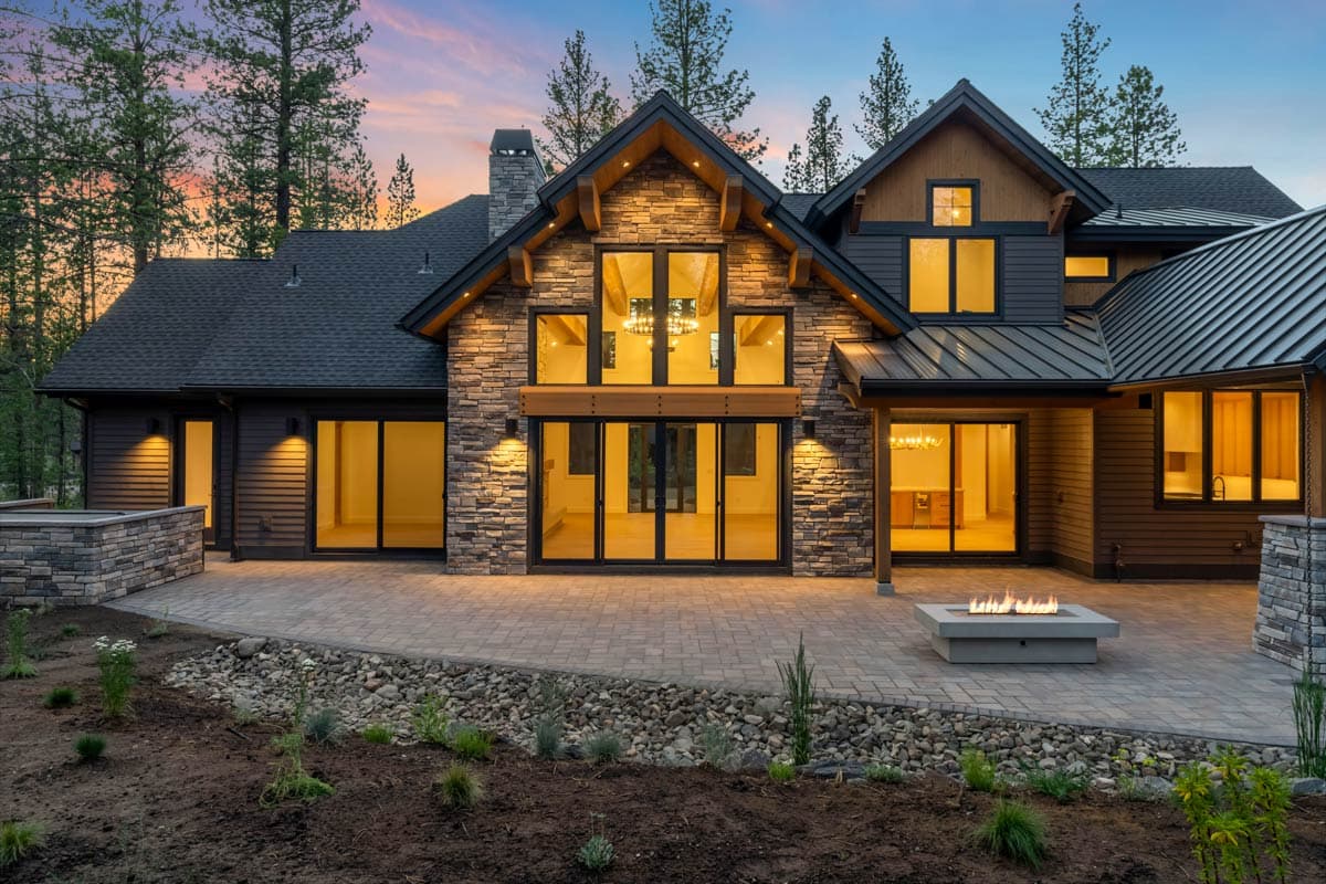 Modern mountain house exterior with stone accents, expansive windows, metal roof, and large patio with fire pit.