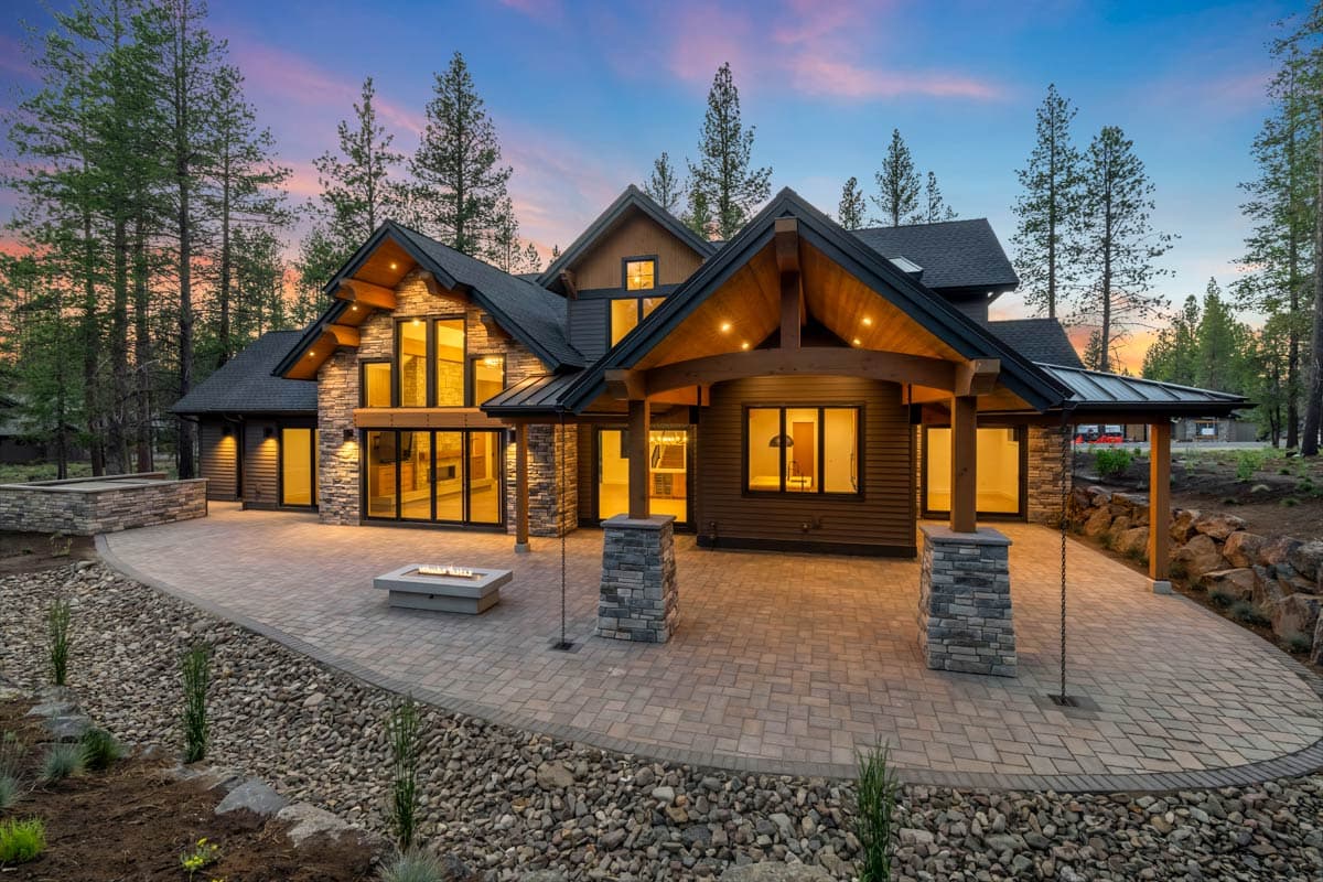 Modern mountain home exterior with stone and wood accents, large windows, covered porch with stone columns, and multi-level rooflines.