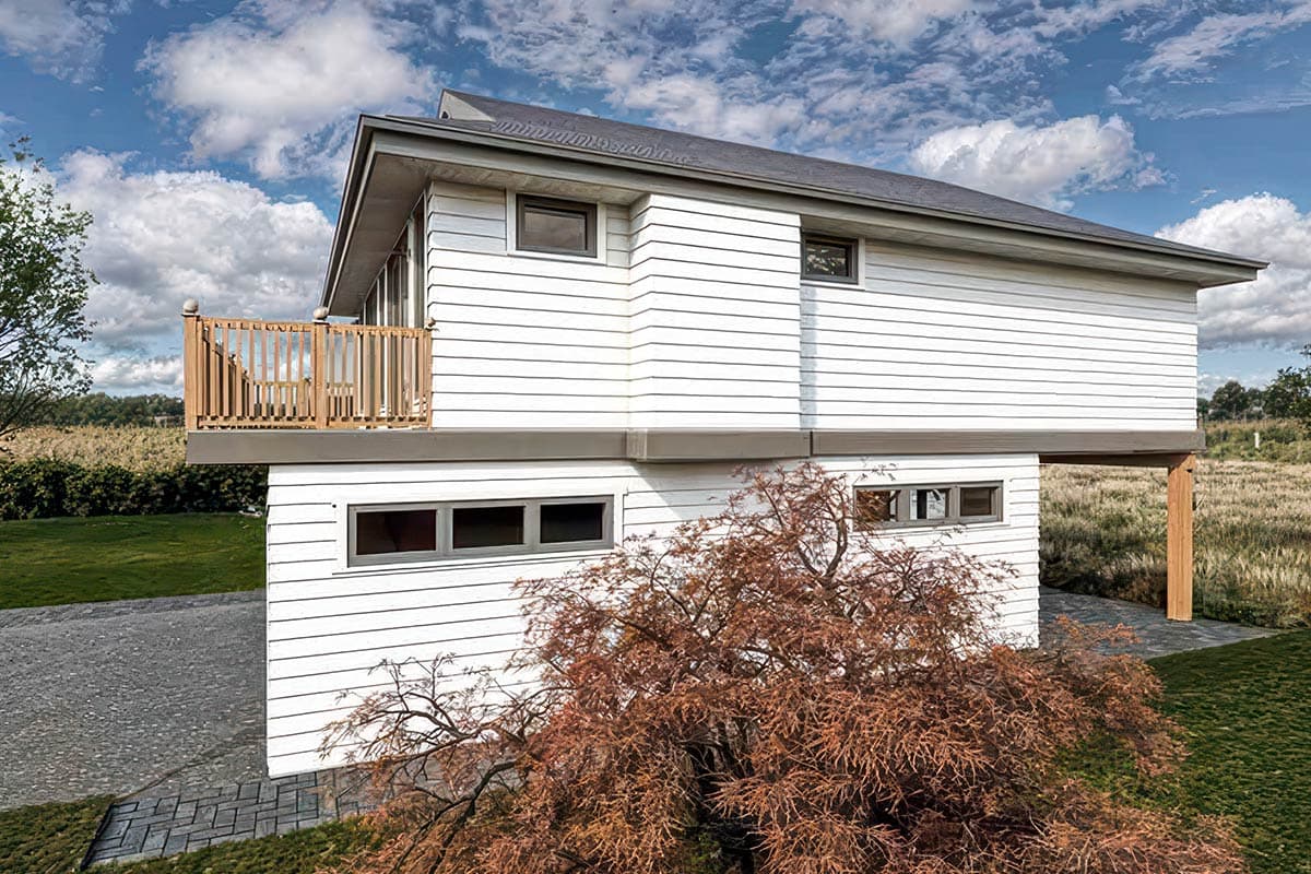 Modern house exterior with horizontal siding, upper-level balcony with wood railing, and a shed roof.