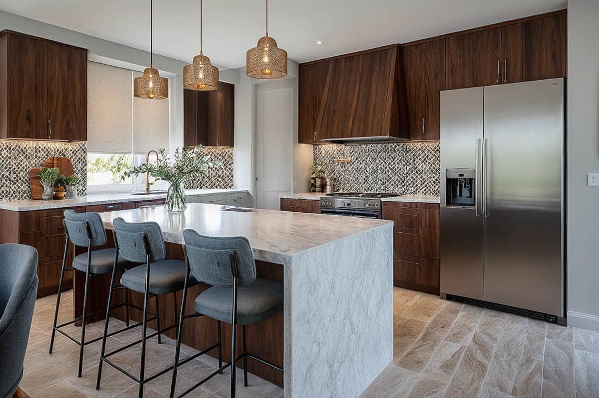 Modern kitchen with dark wood cabinetry, marble island with bar stools, stainless steel refrigerator, and patterned tile backsplash.