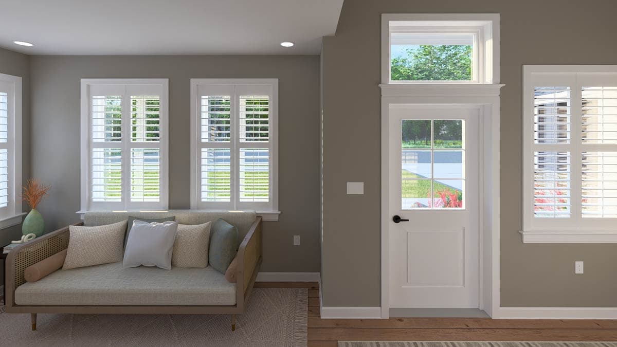 Interior view of a room with a sectional sofa, three large windows with white shutters, and a paneled door with a transom window above.