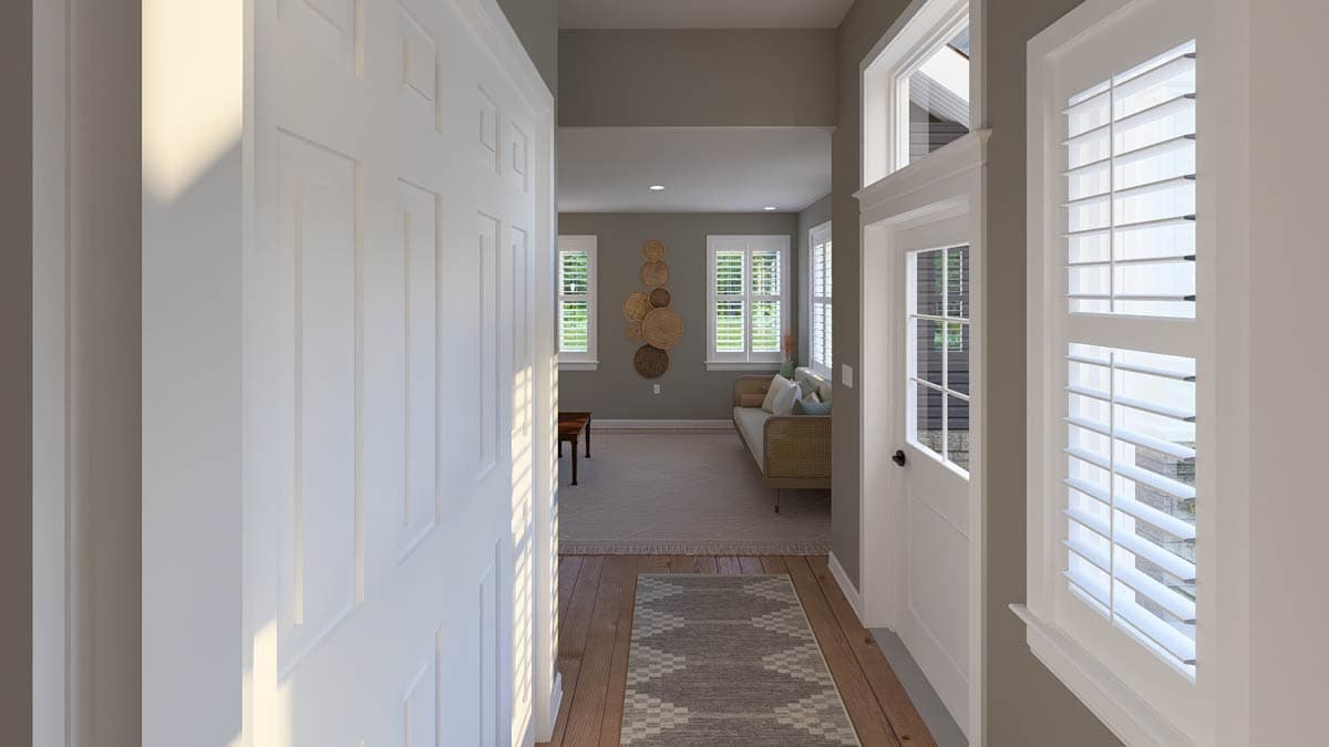 Interior view of a house showing entry hall with paneled doors and a living room with two windows, sofa, and wall decor.