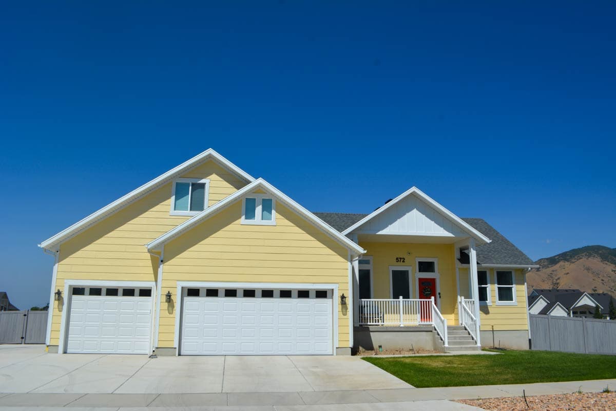 House plan exterior: Two-story yellow house with a prominent gable, two-car garage, and a covered porch with red front door.