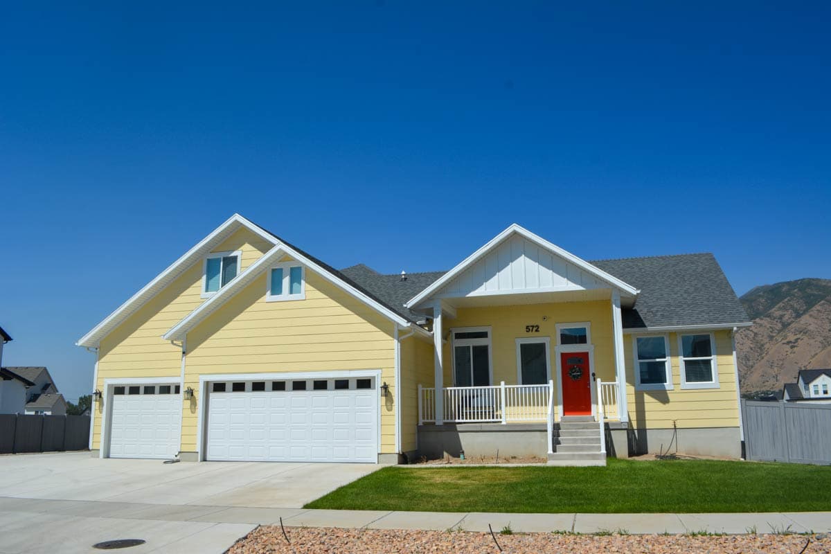 House plan exterior: Yellow two-story home with a white front porch, gable roofline, and a three-car garage.