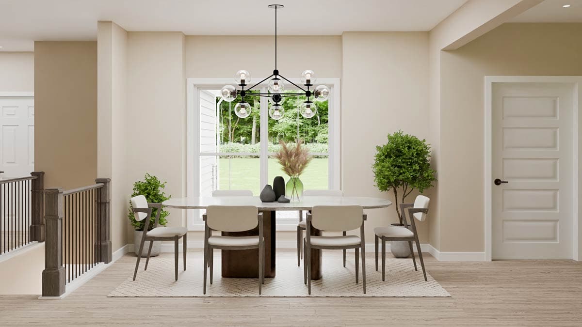 Dining room with oval table, chairs, large window, decorative chandelier, and staircase railing.