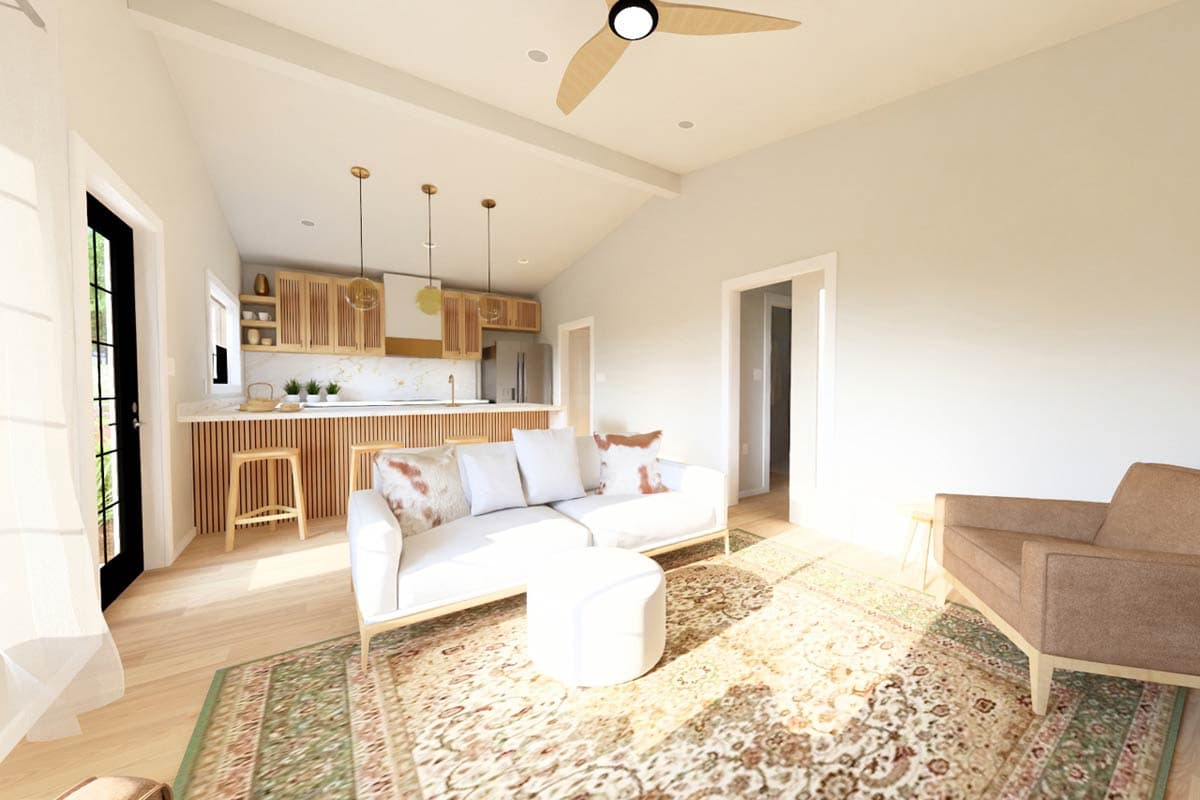 Open-plan living area with vaulted ceiling, kitchen with wood cabinetry, and a white sofa with ottoman.