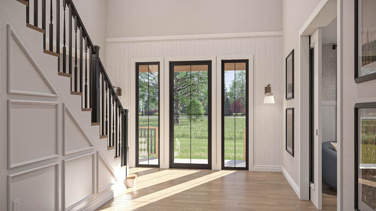 Interior view of entryway with paneled wainscoting, staircase, and three tall windows overlooking a yard.
