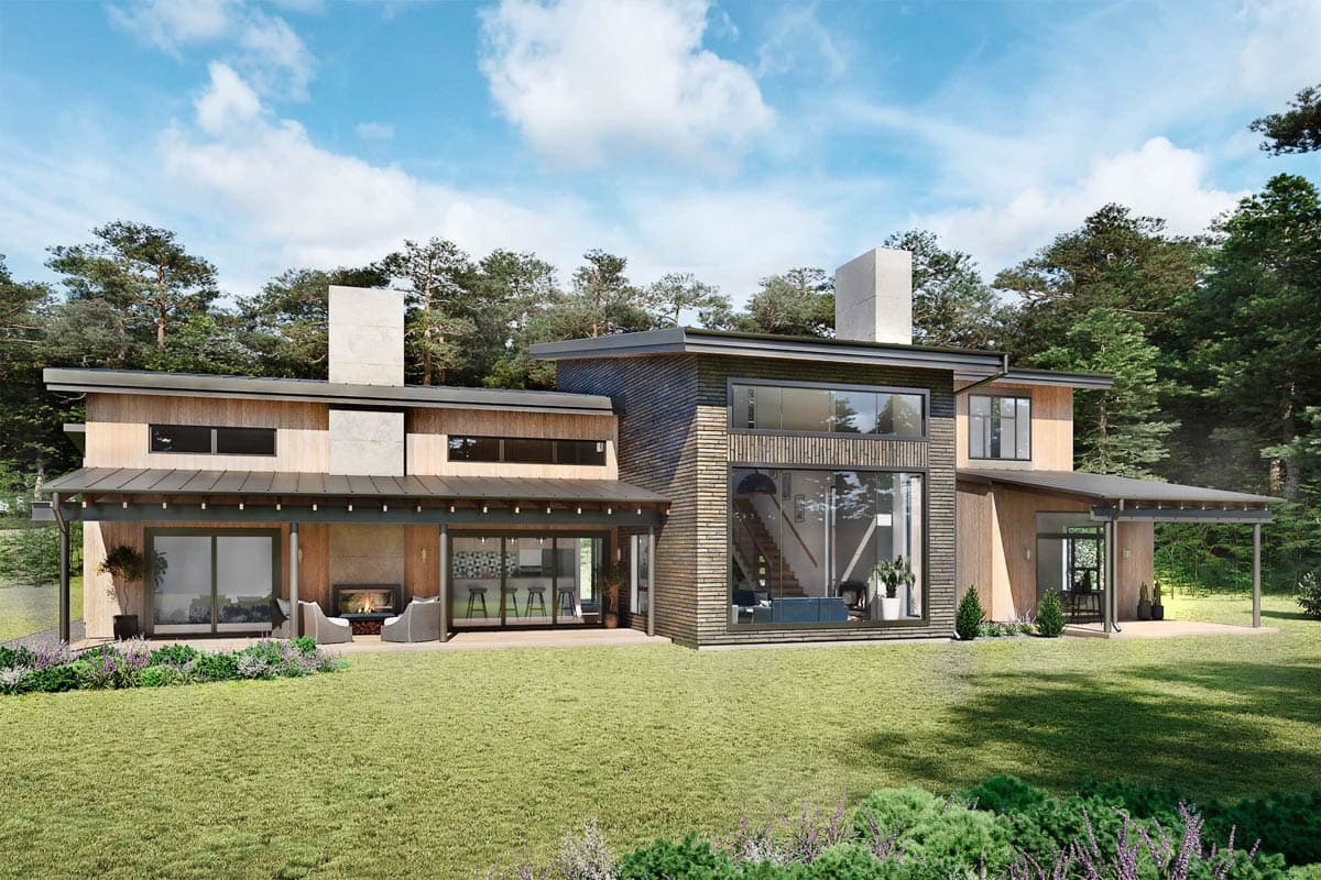 Modern house with wood siding, large windows, and an outdoor fireplace. Set on a grassy lawn with trees in the background.