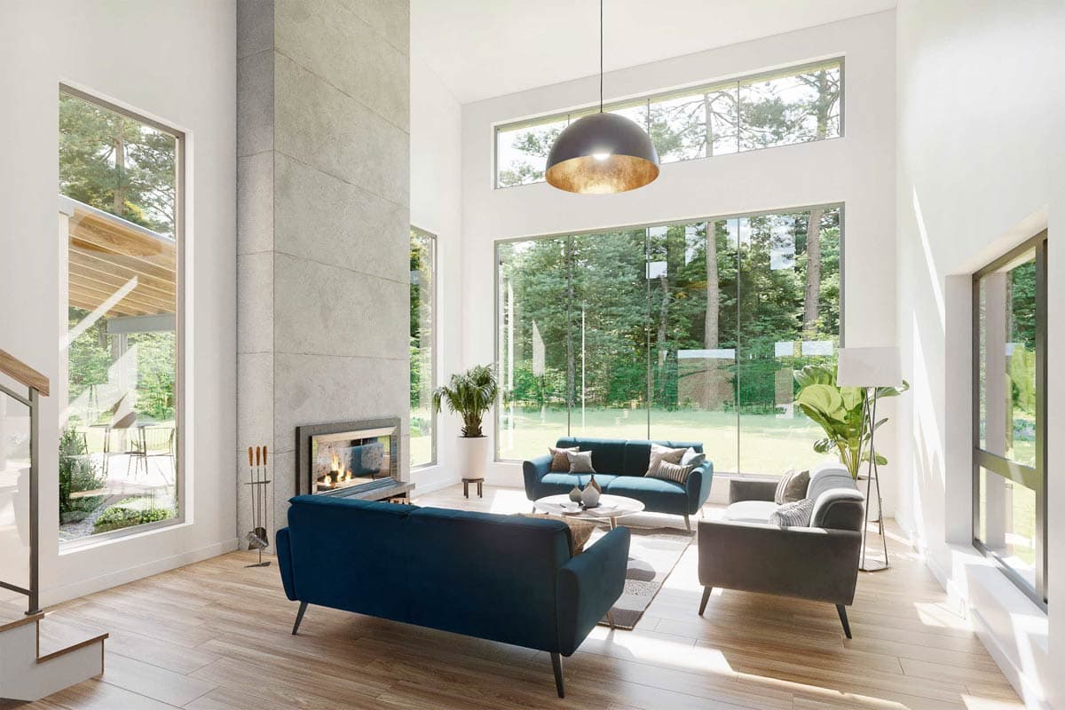 Modern living room with floor-to-ceiling windows and fireplace. Blue sofas, wood floors, and view of trees outside.