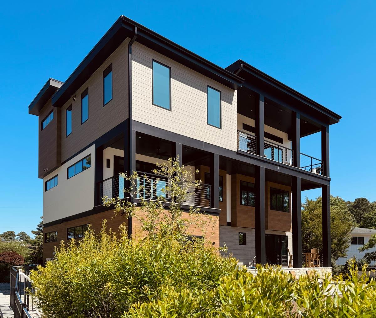 Modern three-story house plan exterior with dark-trimmed windows, stacked materials, and a large covered second-story balcony.
