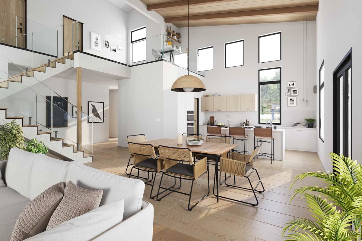 An open-plan interior with a dining area, kitchen, and a staircase. Features high ceilings and lots of natural light.