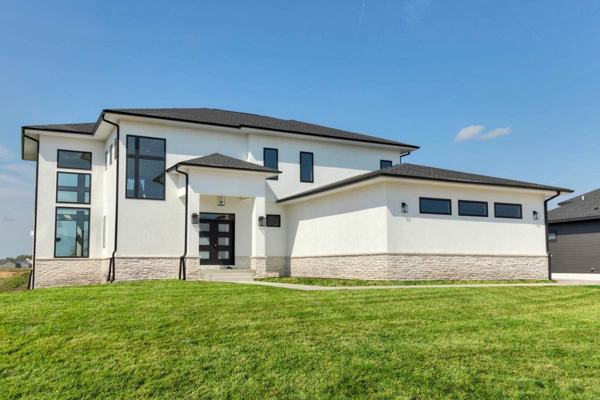 House plan exterior. Two-story modern house with a flat roof, stone veneer accents, and large windows. Includes covered entry and black trim.