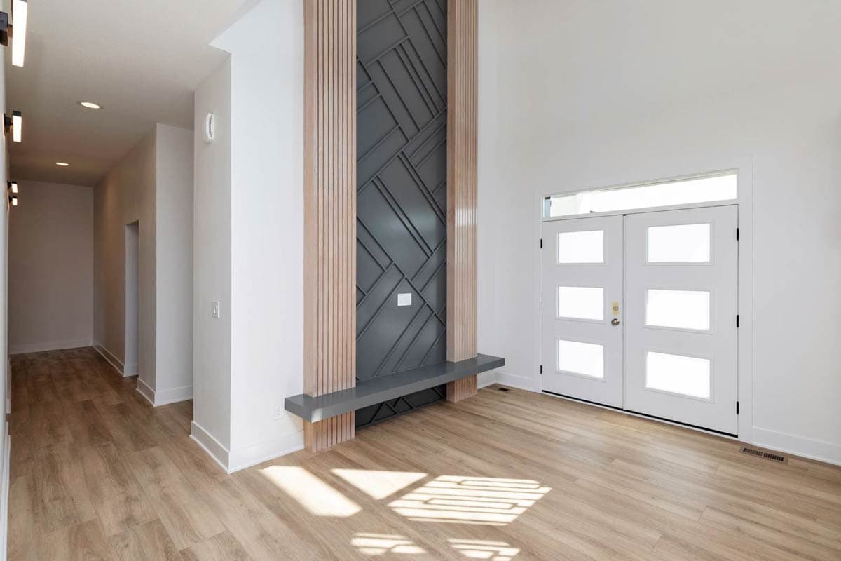 Interior view of entryway with double glass doors, a tall geometric wall feature with wood accents, and a long hallway.