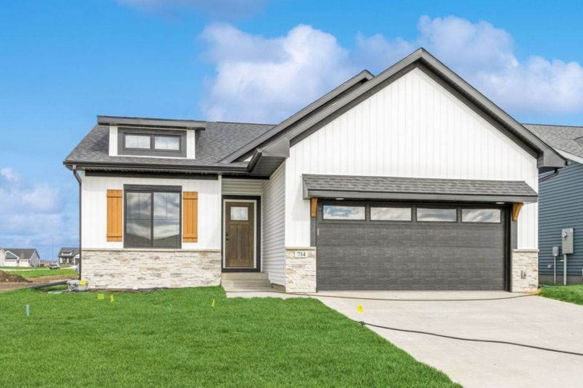 House plan exterior. Ranch style with a gable roof, dormer, and attached garage. Stone facade accents and wood shutters on the front window.