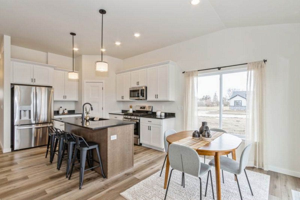 Modern kitchen with island, stainless steel appliances, white cabinetry, pendant lights, and adjacent dining area.
