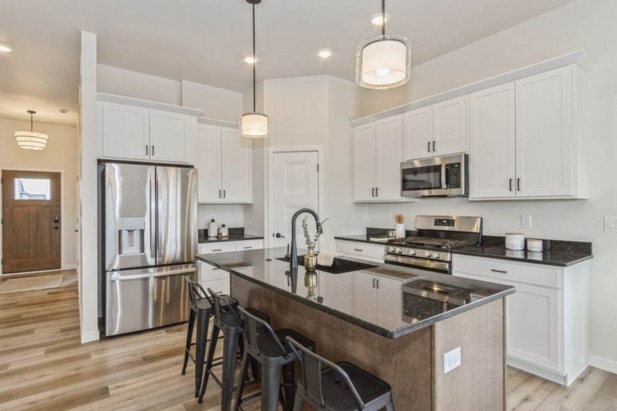 Kitchen with white cabinets, stainless steel appliances, granite countertops, and a large island with seating.