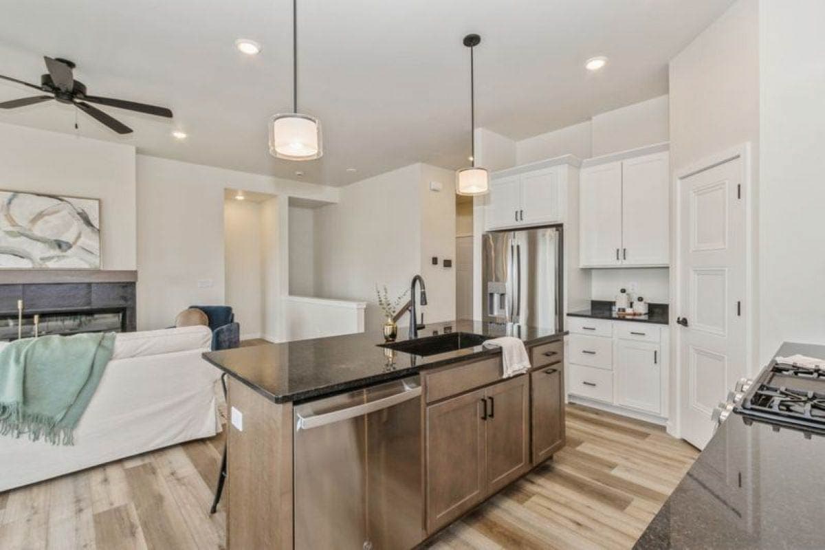 Open-concept kitchen with island, stainless steel appliances, white cabinetry, and adjacent living area with fireplace.