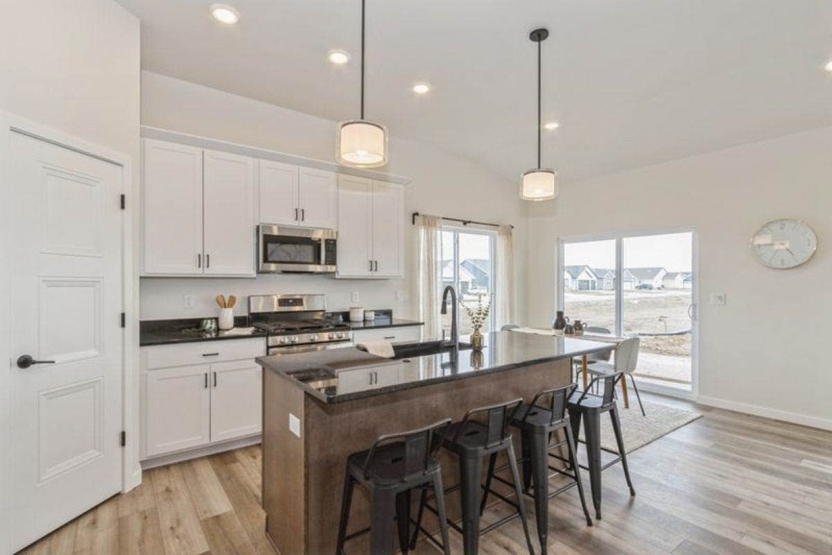 Modern kitchen with white cabinetry, island with seating, stainless steel appliances, and adjacent dining area with sliding glass doors.