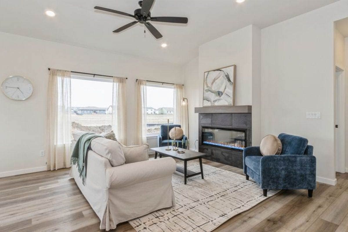 Living room with fireplace, large windows, vaulted ceiling, ceiling fan, and seating areas.