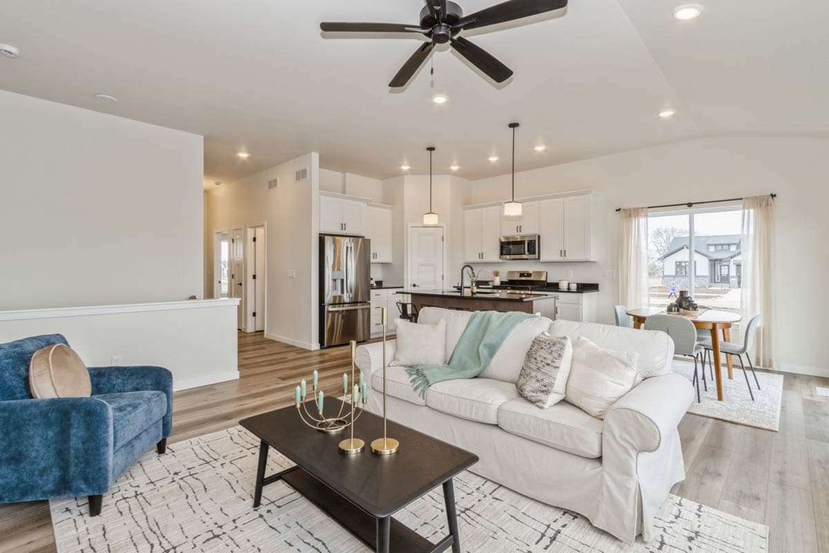 Open concept living area with vaulted ceiling, white sofa, blue armchair, kitchen with island, stainless steel appliances, and dining area.