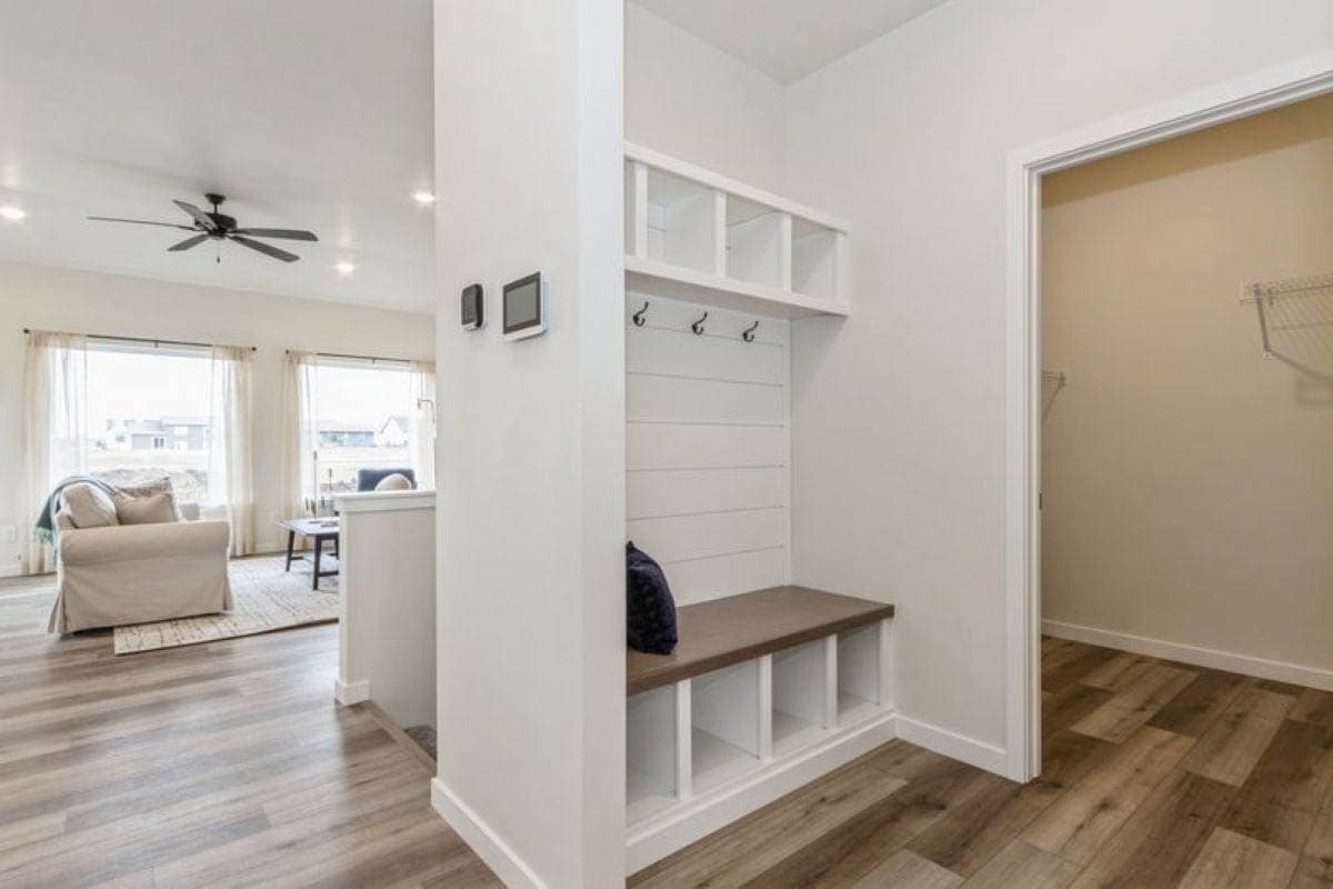 Interior view of mudroom bench with cubbies and hooks, adjacent to living area with large windows.