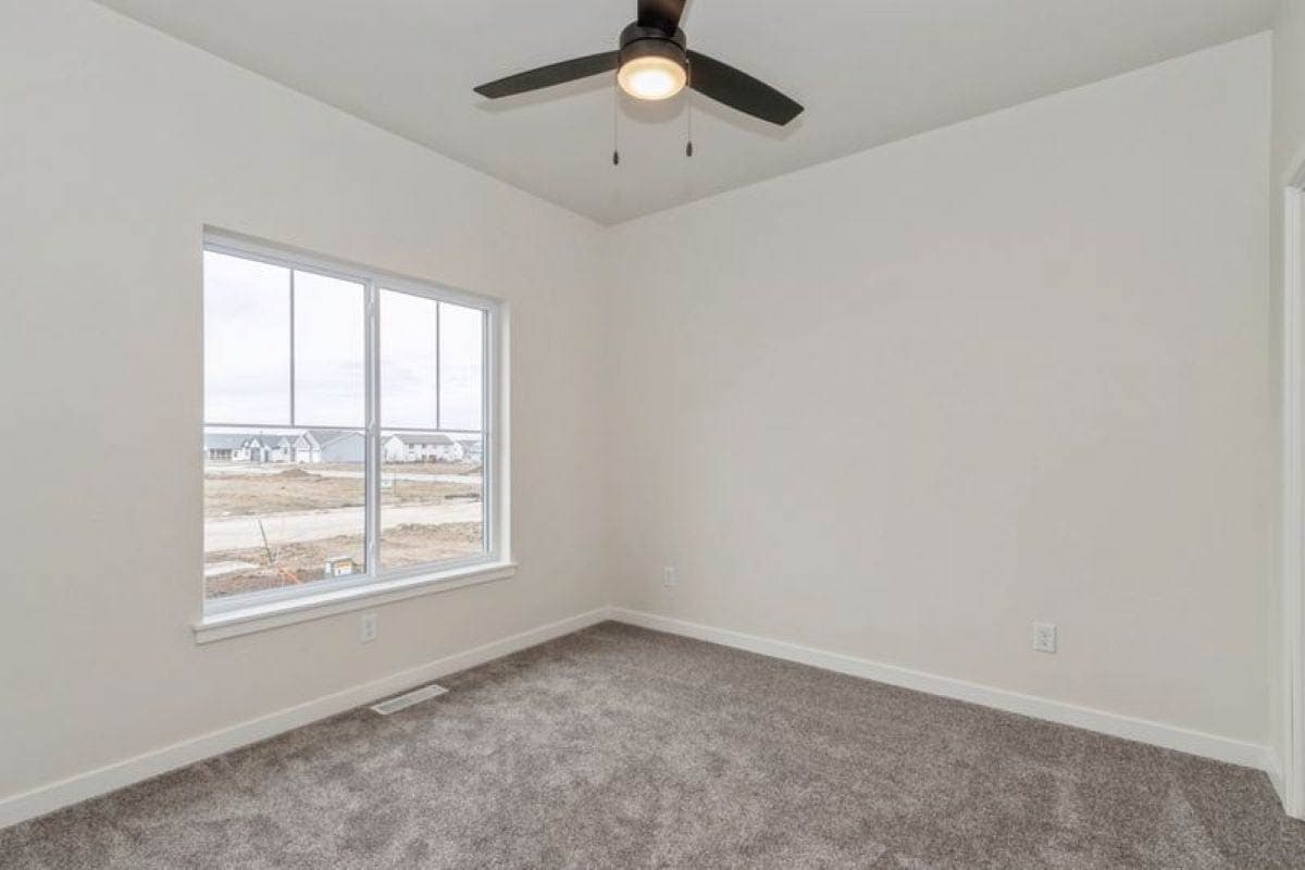 Interior view of a room with carpet, a large window, and a ceiling fan.