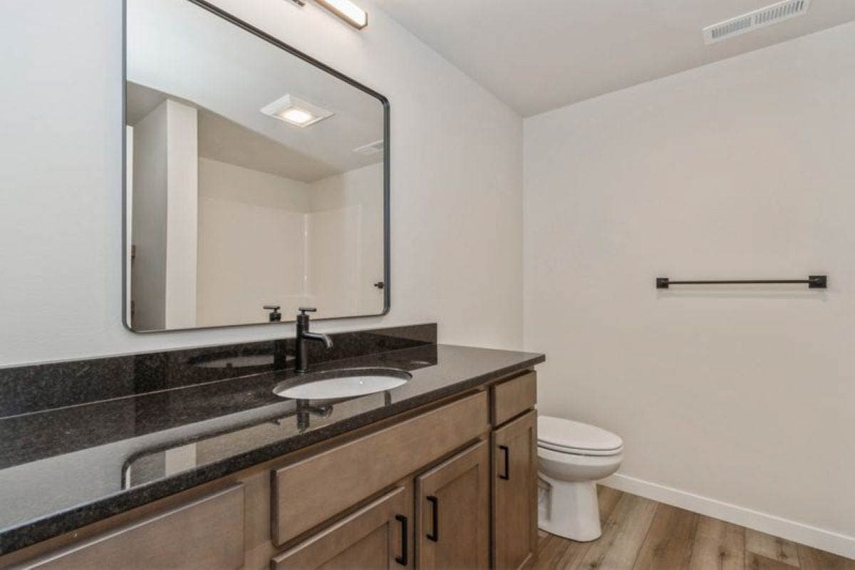 Bathroom with wood vanity, granite countertop, single sink, and toilet. A large mirror hangs above the vanity.
