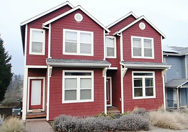 Two-story house plan exterior with red horizontal siding, gable roofs, dormer windows, and a front porch.