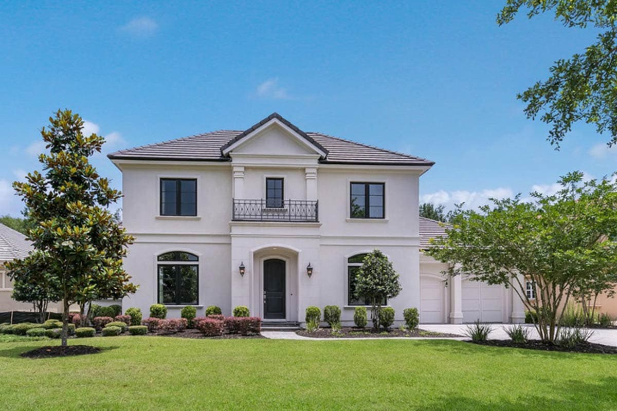 House plan exterior. Two-story Mediterranean style home with a balcony, arched entry, and a side-entry garage. Features a hipped roofline.