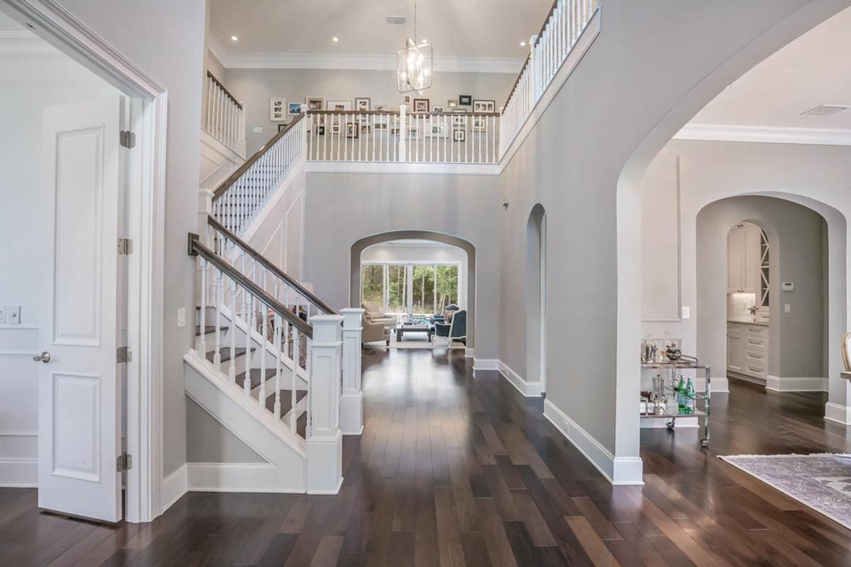 Grand foyer with a two-story open hall, open staircase, and view into a living area through an arched entryway.