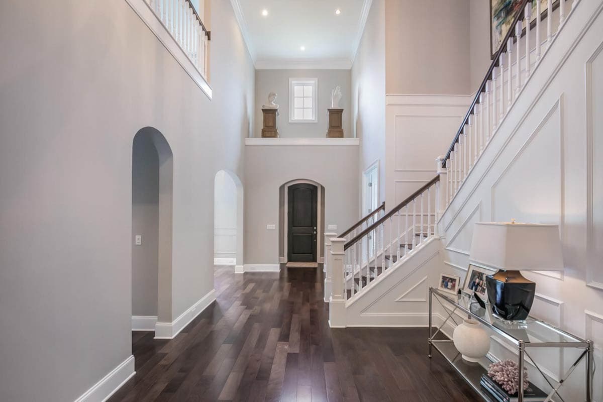 Grand two-story foyer with arched doorways, dark wood flooring, a central staircase, and a dark wood front door.