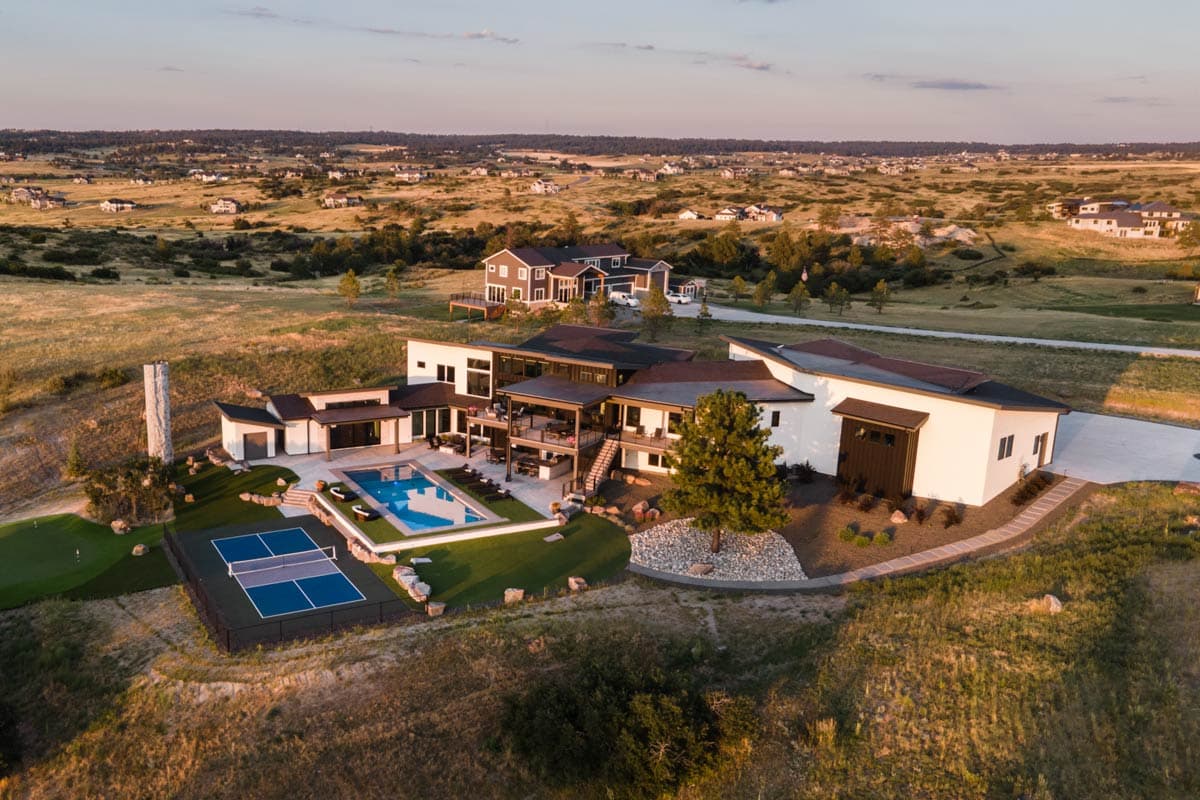 Modern house plan exterior with multiple gables, flat and sloped rooflines, large windows, and expansive patio overlooking pool.