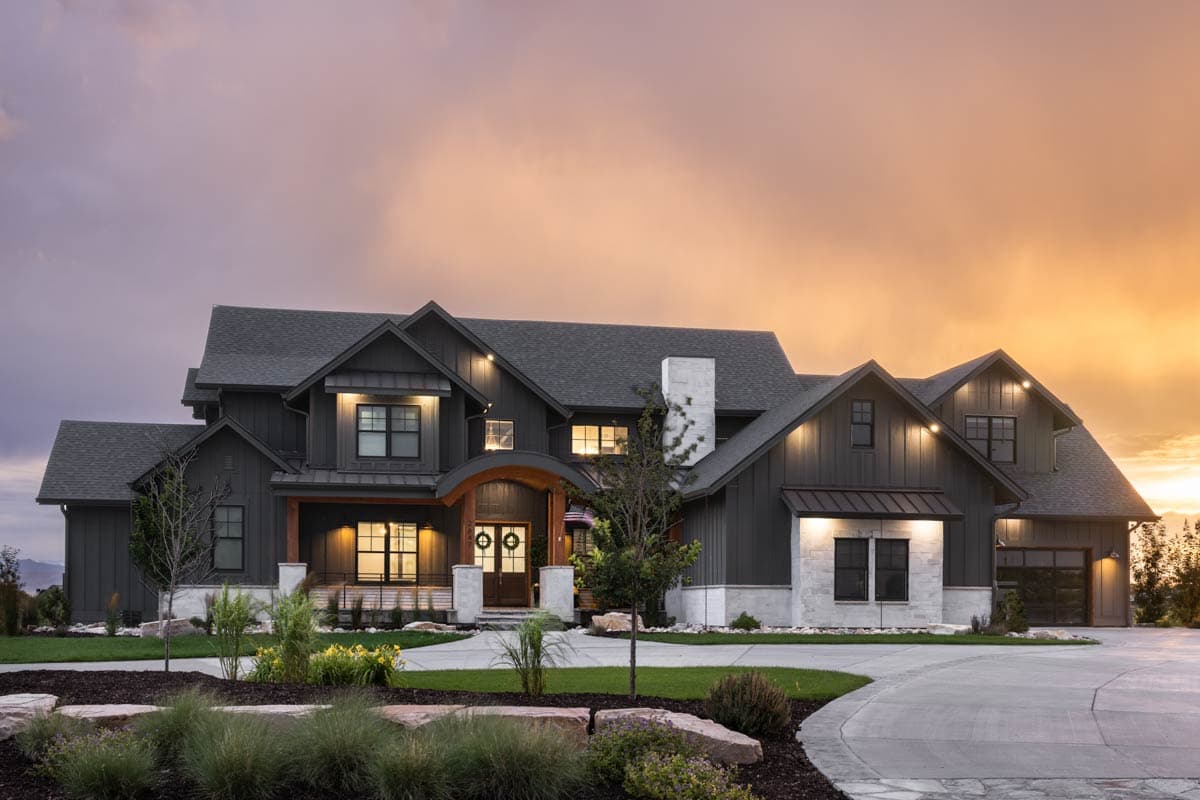 House plan exterior. Two-story Modern Farmhouse with gables, porch with arched entry, and attached garage. Stone and dark siding exterior.