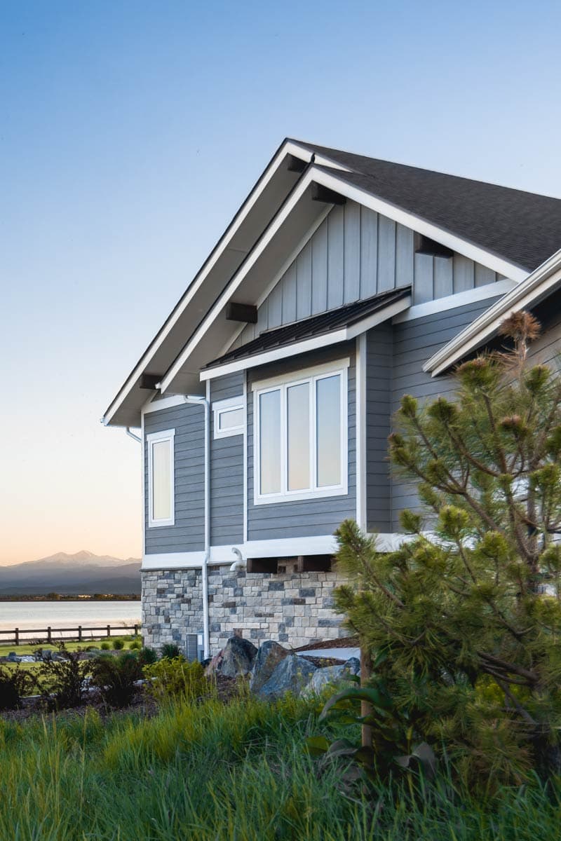 House plan exterior: Modern style, gray siding, stone foundation, gable rooflines, and multiple windows.