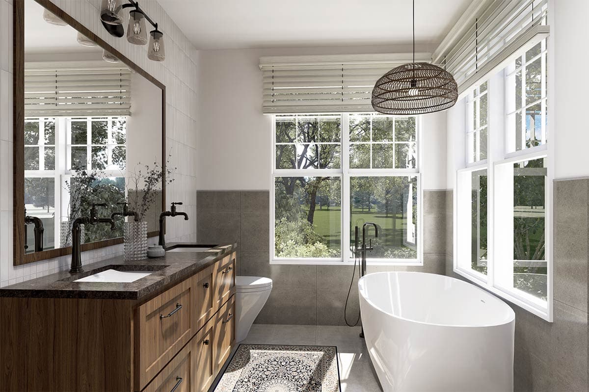 A modern bathroom with a large mirror, wooden vanity, and a freestanding tub. Large windows offer a view of green trees outside.