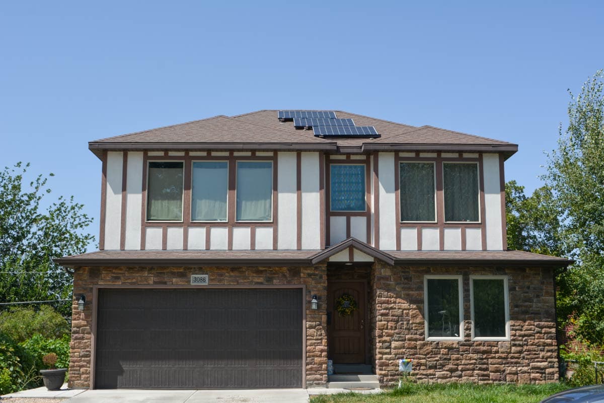 Two-story house plan exterior with stone lower level, faux half-timbering upper level, and solar panels on roof.