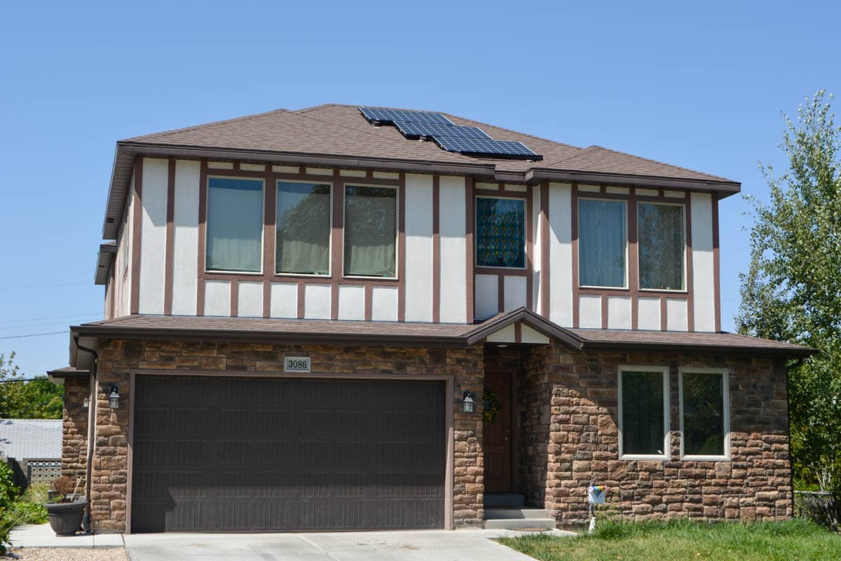 Two-story house plan exterior with stone lower level, Tudor-style upper facade, and solar panels on the roof.