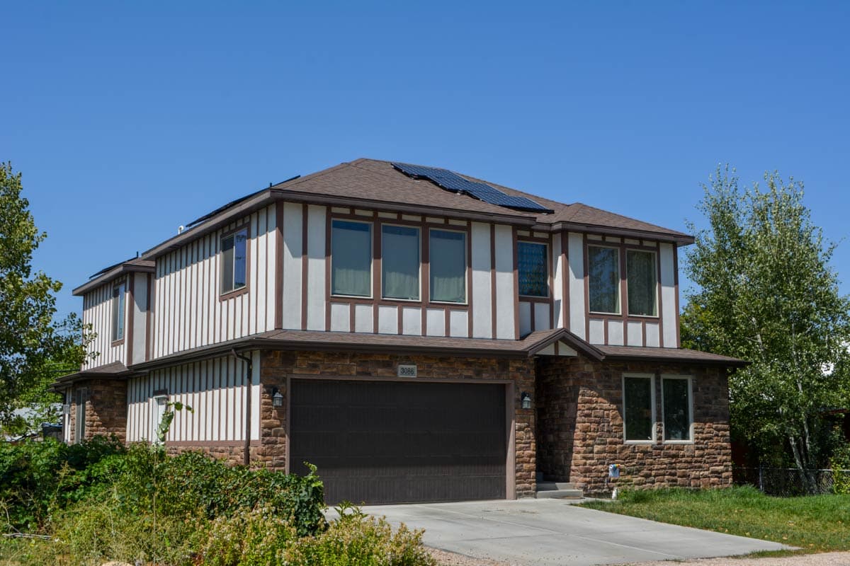 Two-story house plan exterior with stone base, vertical siding, decorative trim, and solar panels on roof.