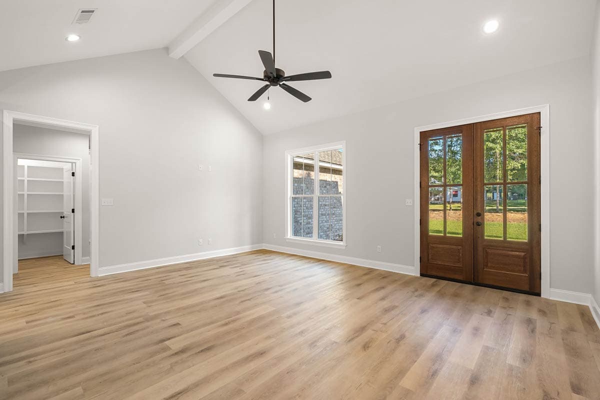 Interior view of living area with vaulted ceiling, fan, window, double doors, and pantry access.
