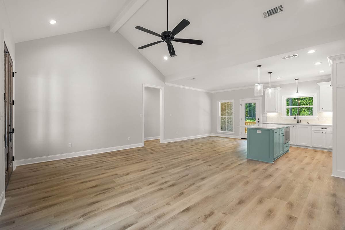 Open concept living area with vaulted ceiling, ceiling fan, kitchen with island, white cabinetry, and double doors.